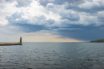 The coast of the Baltic Sea in northern Poland. Seascape: lighthouse stands against dramatic sky, calm water reflecting light, capturing a serene moment before the storm.