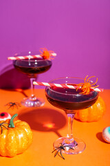 Glasses of delicious red cocktail, pumpkins, spiders and tasty candies for Halloween on color background, closeup
