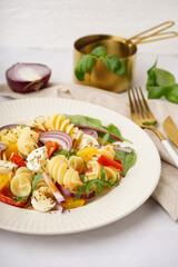 Plate of tasty pasta salad with pepper and red onion on white background