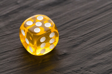 A yellow die, game piece on a dark background