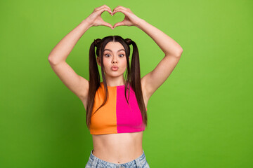 Energetic young woman with bright ponytails in colorful top against green background, expressing...