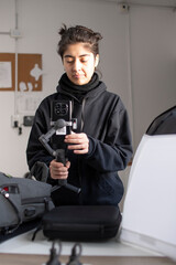 Joven camarógrafo filmando con celular y estabilizador gimbal en interiores enfoque selectivo