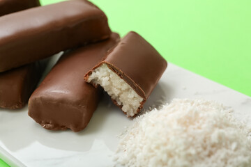 Board with tasty chocolate covered coconut candies on green background