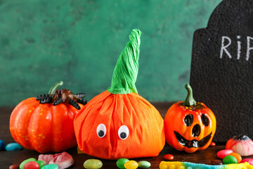 Paper pumpkins for Halloween, grave and tasty candies on wooden table, closeup