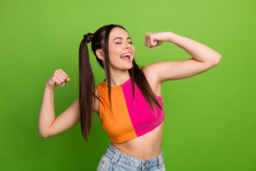 Excited young woman in vibrant outfit celebrating on green background portraying joy, confidence,...