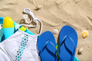Pair of blue flip flops with swimsuit on sandy background