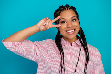 Cheerful young woman posing with a peace sign against a colorful blue background, expressing positivity and joy in a casual outfit
