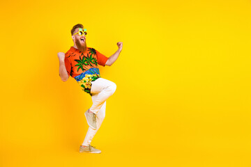 Cheerful bearded man in Hawaiian shirt celebrates on a bright yellow background, expressing...