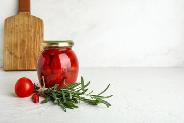Jar of pickled tomatoes with rosemary and chili pepper on white background