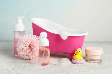 Miniature bathtub with bath foam, cosmetic products and rubber duck on white grunge background