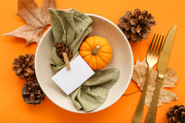 Autumn table setting with pumpkin, leaves and golden cutlery on orange background