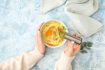 Woman adding spices into bowl with tasty chicken soup on blue background
