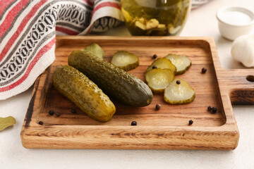 Wooden board with tasty canned cucumbers on white background