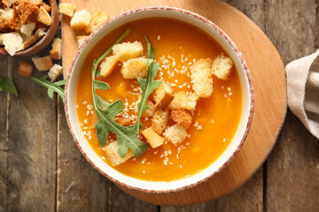 Bowl of delicious pumpkin cream soup with croutons and arugula on wooden background