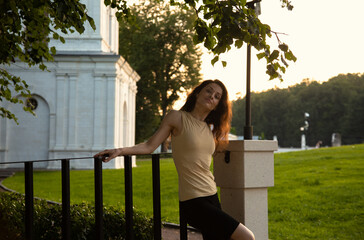 Naklejka premium Beauty happy face woman, enjoying fresh air standing under the tree in a city street park at white column. Female brunette model relax in summer day with smiling face with long brown hair.