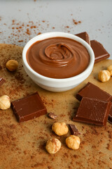 Composition with bowl of tasty melted chocolate and nuts on light background, closeup