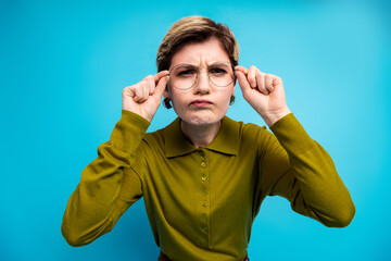 Young stylish woman with a short haircut wearing khaki shirt and glasses against a blue background...