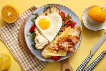 Composition with tasty fried egg, cut croissant, bacon, tomatoes and glass of juice on yellow background