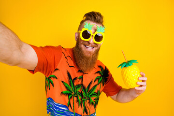 Cheerful man wearing tropical themed attire holding a pineapple drink against a vibrant yellow...