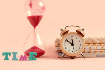 Word TIME, alarm clock and hourglass on pink background