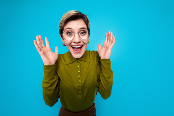 Cheerful young woman with short hair and glasses expressing excitement against a vibrant blue...