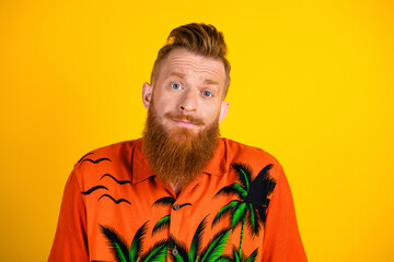 Young man with vibrant beard wearing tropical shirt posing against yellow background expressing a...
