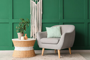 Stylish armchair, coffee table and houseplant near green wall in living room