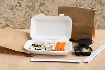 Plastic container with tasty sushi rolls, chopsticks and paper bags on beige grunge background....