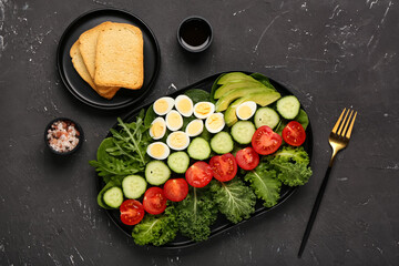 Plate of fresh salad with boiled quail eggs, soy sauce and toasts on dark background