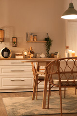 Interior of modern kitchen with glowing lamps, white counters, table and chair at evening