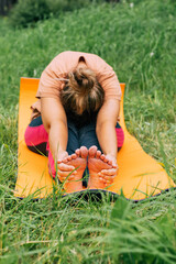 Adult female practicing yoga forward bend outdoors on yellow mat