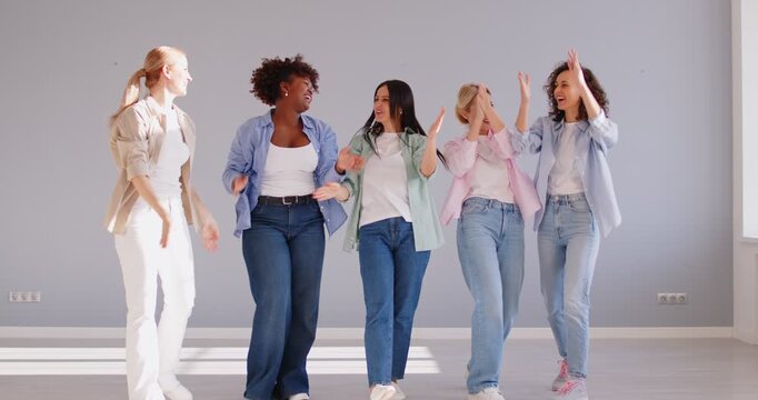 Group of multiethnic happy women holding hands up and smiling on grey wall background. Female friends in casual clothes standing in a row clapping hands. Teamwork concept. 4k video. Slow motion video
