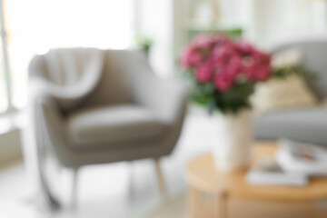 Blurred view of living room with armchair and flowers in vase