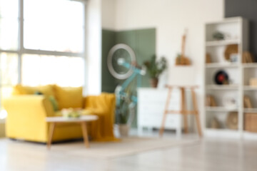 Interior of stylish living room with yellow sofa, coffee table, canvas and bicycle, blurred view