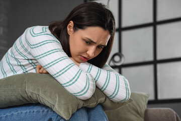 Depressed young woman with pillow sitting on couch at home