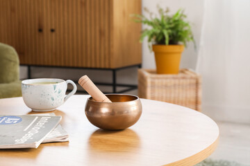 Tibetan singing bowl with cup and magazines on table in living room, closeup