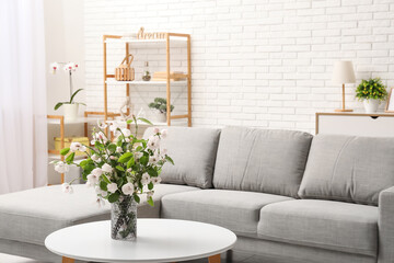 Stylish living room with grey sofa, coffee table and bouquet of blooming tree branches
