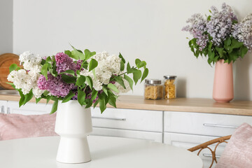 Vases with beautiful lilac flowers in kitchen