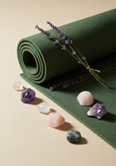 A green yoga mat with lavender sprigs and an assortment of crystals on a beige background surface