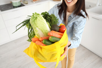 Young Asian woman with yellow shopper bag full of fruits and vegetables in kitchen