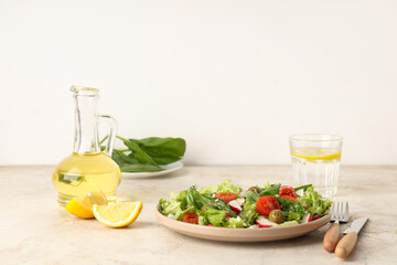 Plate with tasty salad, glass of water and oil on light table