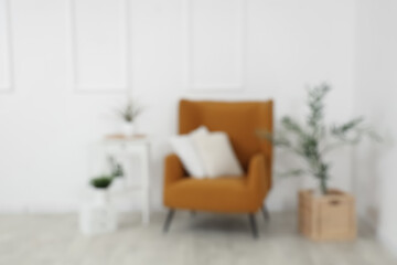 Stylish interior of living room with brown armchair, pillows, coffee table and houseplant, blurred view