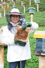Guatemalan woman holding a beehive in a white beekeeping suit 