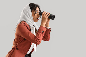 Fototapeta premium Female African-American spy looking through binoculars on light background