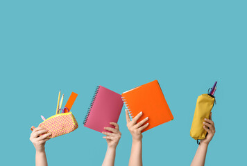 Female hands holding notebooks and pencil cases with stationery on blue background