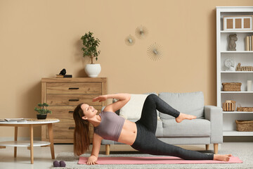 Beautiful young woman practicing yoga on mat in living room