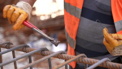 Construction worker bending and tying steel rebar with pliers for reinforced concrete structure at building site