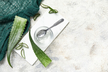 Glass bowl of aloe vera gel and leaves on grunge background