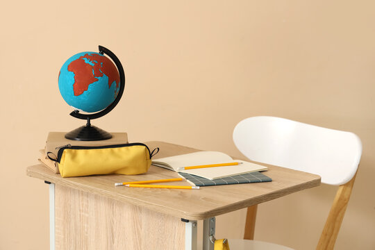 School desk with backpack, globe and notebooks in classroom