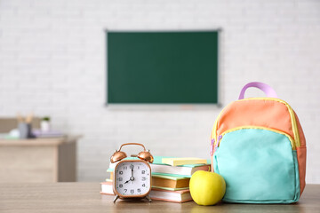 Apple, alarm clock, books and schoolbag on desk in classroom. Back to school concept